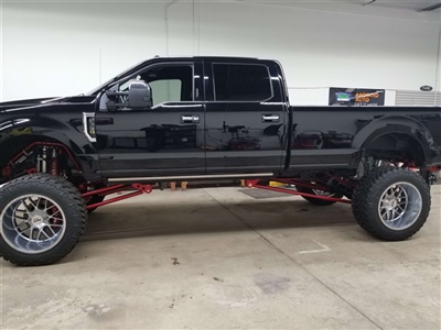 Lifted black pickup truck with large, shiny wheels and red suspension components, parked in a garage.
