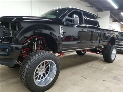 Lifted black pickup truck with large, shiny wheels and red suspension components, parked in a garage.