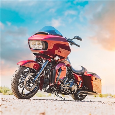 A red touring motorcycle parked outdoors on a sunny day, featuring a large front fairing, saddlebags, and chrome accents.