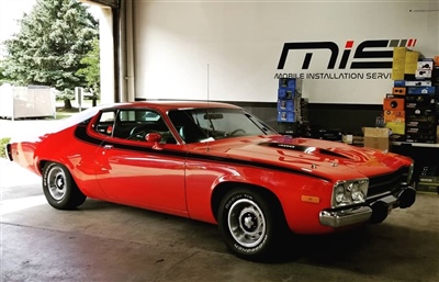 Red classic muscle car parked inside a garage with "Mobile Installation Services" signage on the wall in the background.
