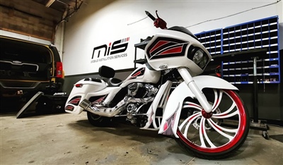 A custom white motorcycle with red accents and large, decorative wheels, parked indoors next to a black vehicle, with "MS" logo on the wall in the background.