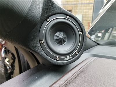 A close-up view of a car speaker installed on the dashboard near the windshield.