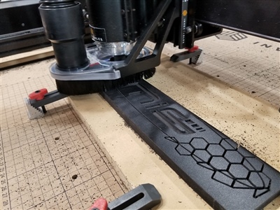 A close-up view of a CNC machine in operation, cutting a design into a piece of material secured to the worktable with clamps.