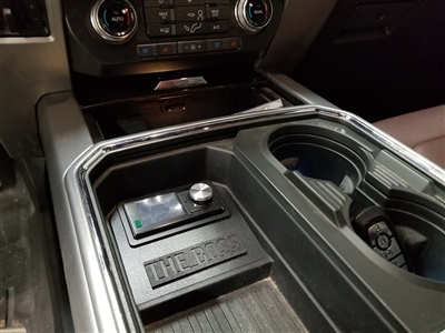 A close-up view of a car's center console featuring cup holders, a small storage compartment, and control buttons for the vehicle's functions.