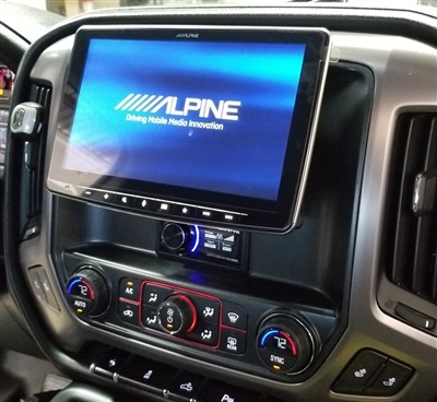 Vehicle dashboard featuring a large Alpine touchscreen display, control buttons, and climate control knobs below.