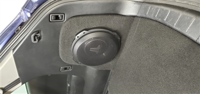 A close-up view of a car's trunk interior showing a subwoofer installed on the side panel.