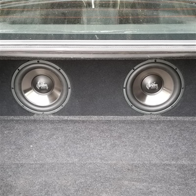 A close-up view of two subwoofers installed in the rear deck of a car, visible through the back window.