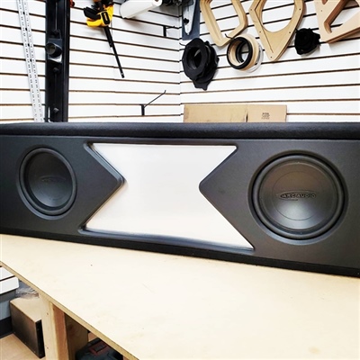 A custom speaker enclosure with two subwoofers and a distinctive central design, displayed on a workbench in an audio shop.