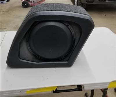 A custom carpeted subwoofer enclosure with the subwoofer installed, placed on a workbench in a garage or workshop.
