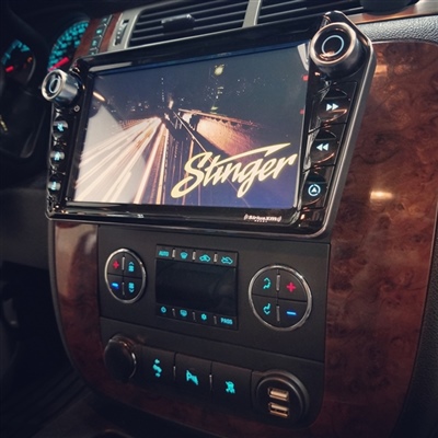 Vehicle dashboard featuring a large Stinger touchscreen display, surrounded by wood-grain paneling, with climate control buttons and knobs below.