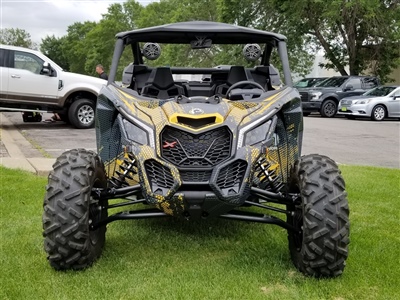 A front view of a black and yellow off-road vehicle with large tires and an aggressive design, parked on a grassy area with other vehicles in the background.