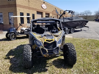 A black and yellow off-road vehicle parked on grass outside a brick building, with a customized golf cart and a boat on a trailer in the background.