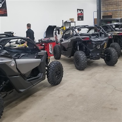 A workshop with several off-road vehicles lined up, some with their hoods open and a person working in the background.