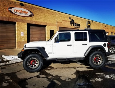 White Jeep Wrangler with custom wheels parked outside a building with "Mobile" and "Proto" signage on the wall.