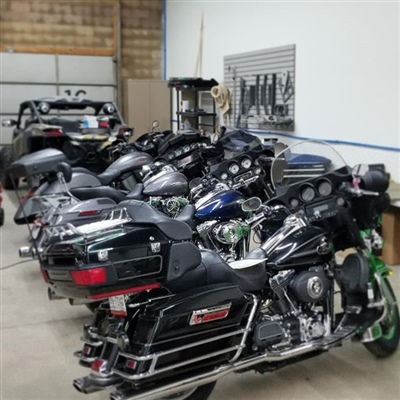  Several motorcycles parked in a row inside a garage, with a car visible in the background.
