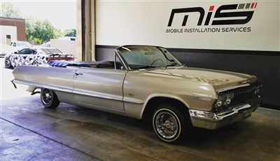 Classic convertible car parked inside a garage with "Mobile Installation Services" signage on the wall in the background.