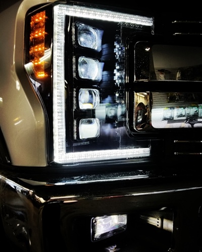 Close-up of a vehicle's front headlight assembly with LED lights, including a vertical row of amber lights and a bright white surround. The chrome bumper and additional lights are visible below.