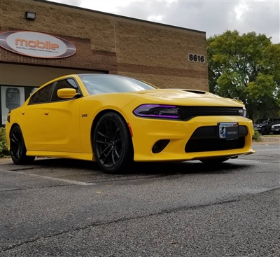 Yellow Dodge Charger parked outside a building with "Mobile" signage on the wall in the background. The car features black wheels and tinted windows.