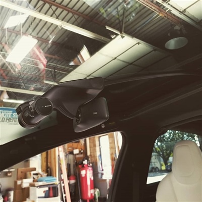 Interior view of a car, focusing on a black device mounted near the rearview mirror, with a garage background.