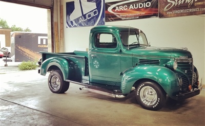 A vintage green pickup truck parked inside a garage with banners hanging on the wall in the background.