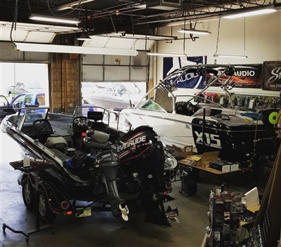 A garage with multiple boats being worked on, including a black boat with an outboard motor and a white boat in the background.