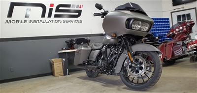 A matte gray motorcycle parked inside a garage with "Mobile Installation Services" sign on the wall in the background.