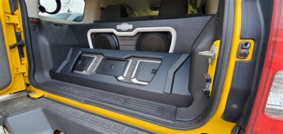 Rear view of a yellow vehicle showcasing a custom audio system with speakers and amplifiers installed in the trunk.
