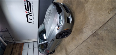 A silver car parked inside a garage with "Mobile Installation Services" sign on the wall in the background.