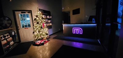 A dimly lit office reception area decorated for Christmas, featuring a lit Christmas tree and a reception desk with a glowing purple logo.