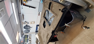 A vehicle's headliner removed and placed on a workbench inside a garage, surrounded by various tools and equipment.