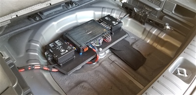 Interior of a vehicle's trunk with exposed battery and wiring components, showcasing the vehicle's electrical setup.