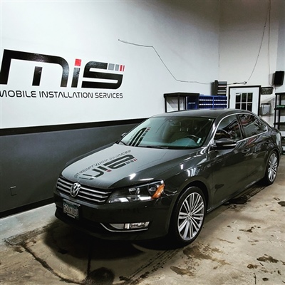 Black Volkswagen sedan parked inside a garage with "Mobile Installation Services" signage on the wall in the background.