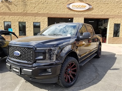 A black Ford pickup truck with custom rims parked in front of a brick building with a "Mobile" sign above the entrance.