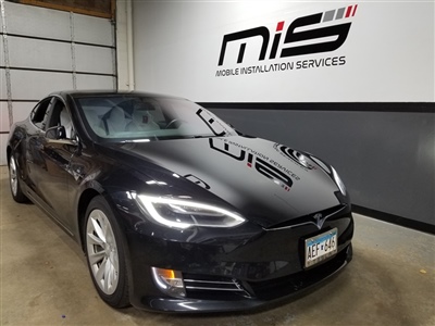  A black Tesla parked inside a garage with "Mobile Installation Services" sign on the wall in the background.