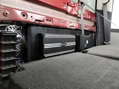 Interior of a vehicle showing an installed amplifier and wiring setup behind the rear seats, with the seatbacks folded down.