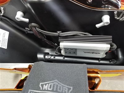 Close-up view of a Harley-Davidson motorcycle compartment showing an installed audio amplifier and wiring setup.