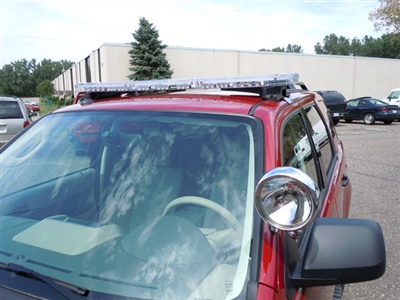Front view of a red vehicle with a roof-mounted light bar and a large spotlight attached to the driver's side mirror, parked outside a building.
