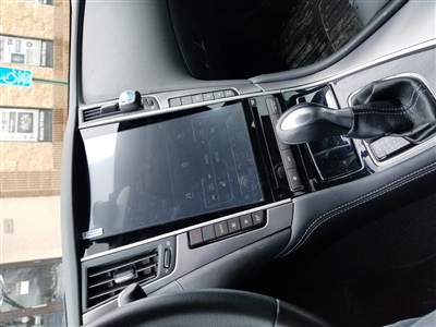 Close-up of a car's center console featuring a large touchscreen display, control buttons, and a gear shifter, with part of the dashboard visible.