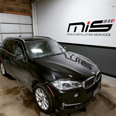 Black BMW SUV parked inside a garage with "Mobile Installation Services" signage on the wall in the background.
