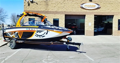 A sleek, white and orange speedboat on a trailer is parked outside a brick building with a sign above the entrance.