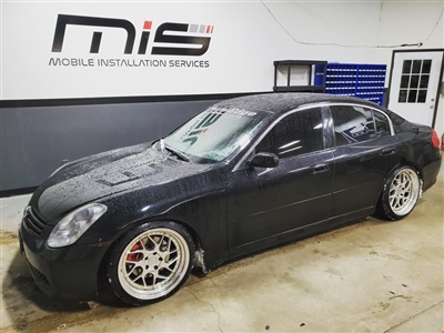 Black sedan with custom rims parked inside a garage with "Mobile Installation Services" signage on the wall in the background.