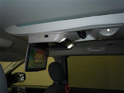 A close-up view of a ceiling-mounted screen inside a car, displaying a "DVD Player" message, with part of a headrest visible below.