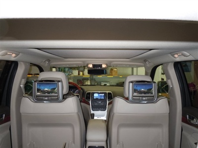 The interior of a car with beige seats, showing two screens mounted on the back of the front seats displaying multimedia content, and a central touchscreen display on the dashboard.