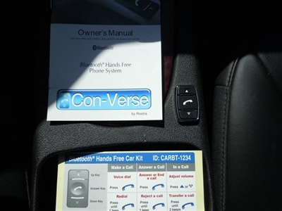 A car's center console showing an owner's manual, a remote control, and a guide for a Bluetooth hands-free car kit labeled "Con-Verse."