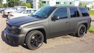 A matte black SUV parked in a lot with other vehicles in the background.